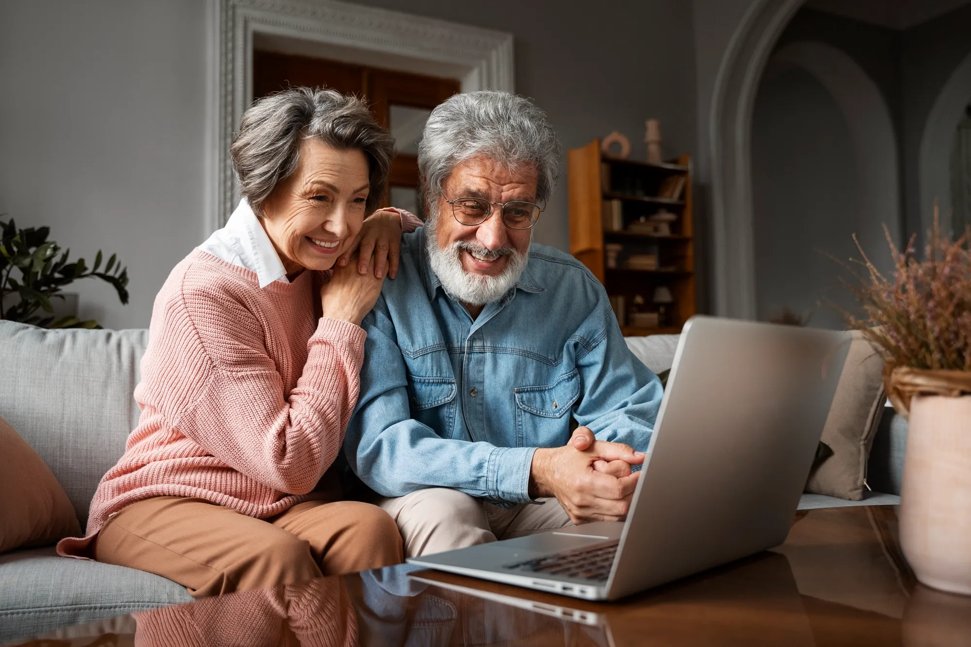 An older couple sitting together on their sofa, looking at a laptop