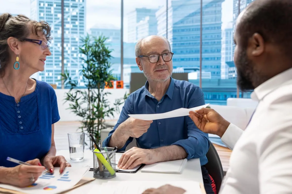 An adviser handing a document across a meeting table to an older couple