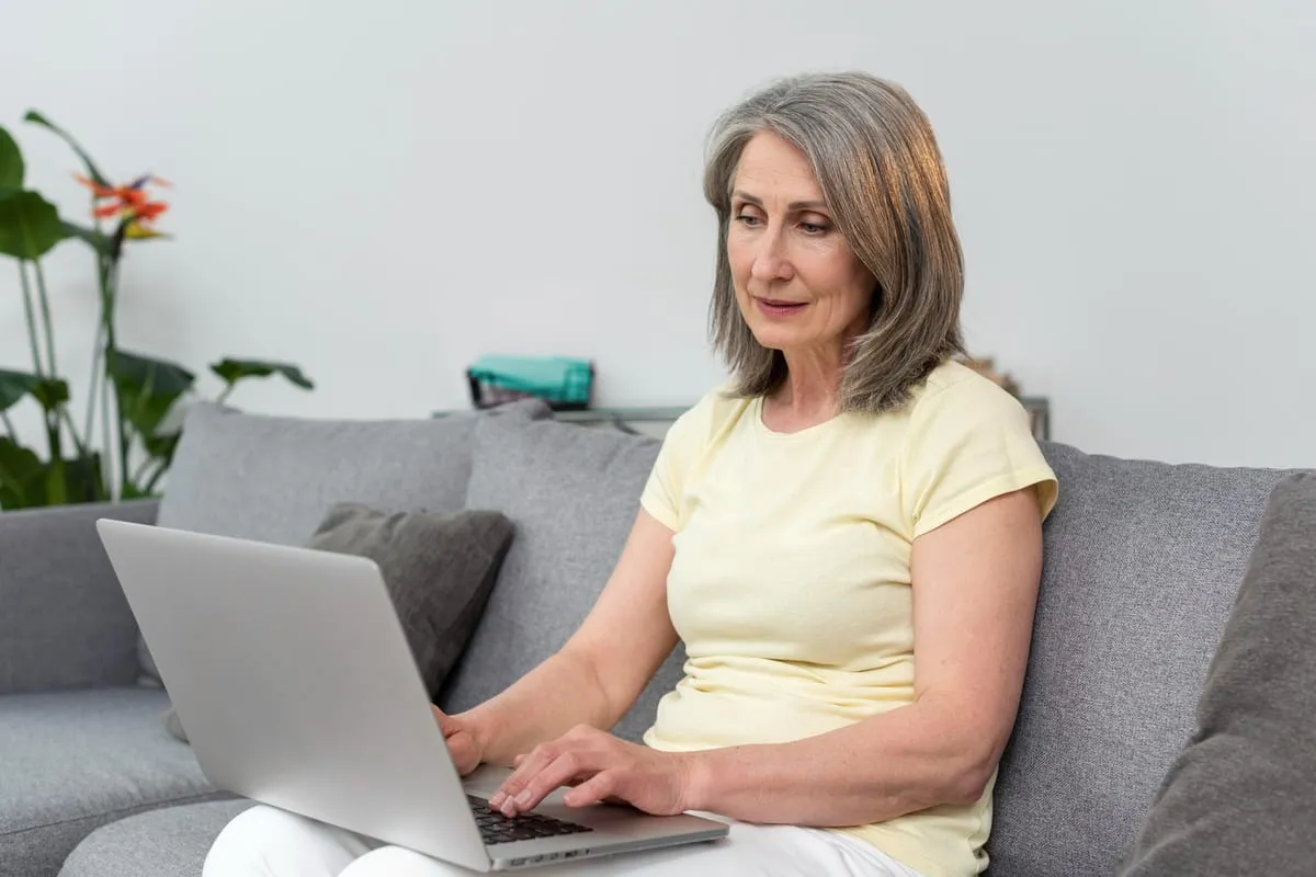 An older woman reading on a laptop at home