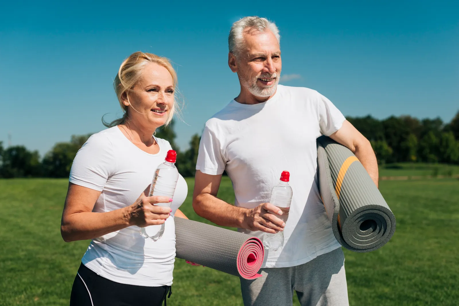 A couple carrying exercise mats across a park