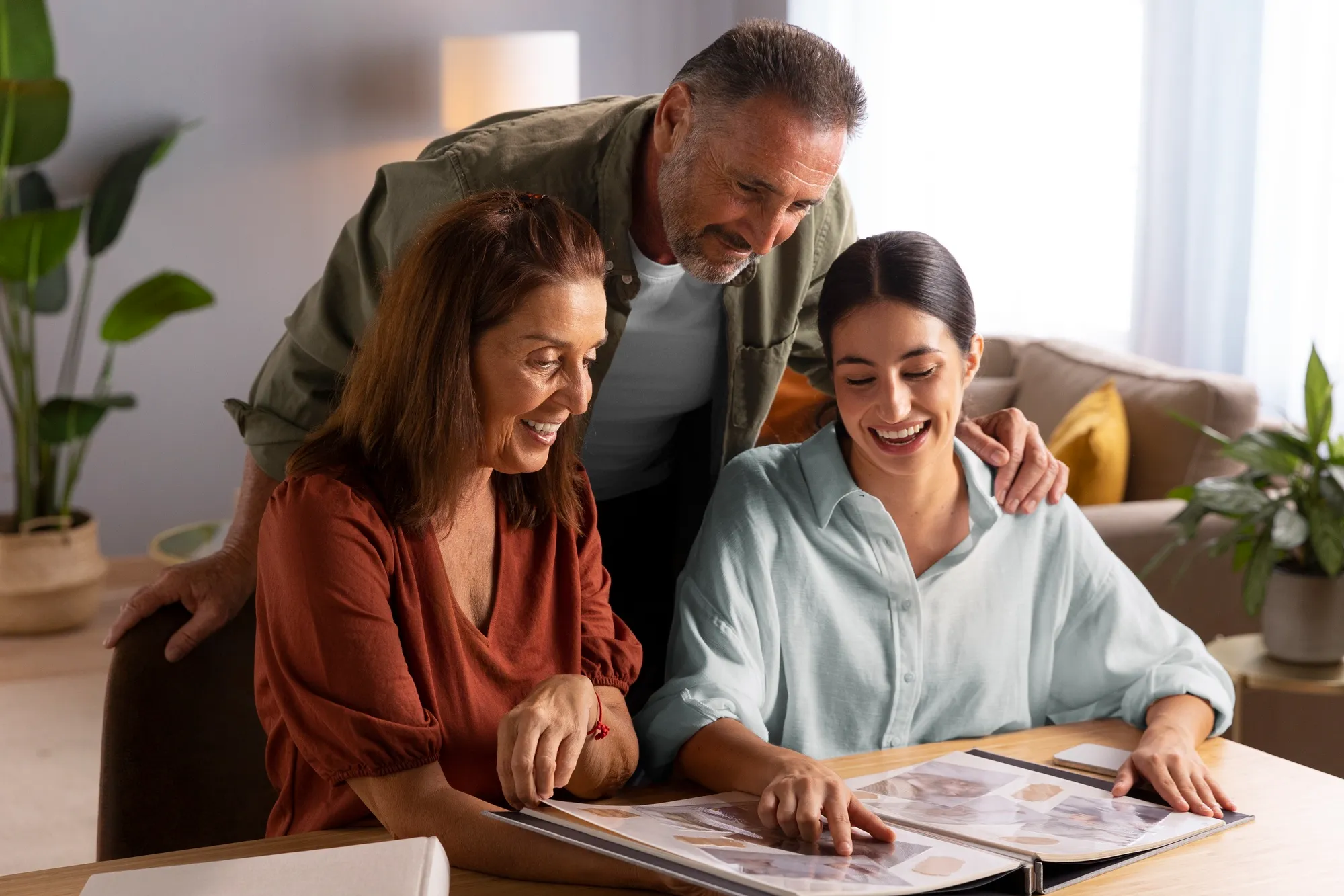 Three family members at home, smiling together over an open photo album on the table
