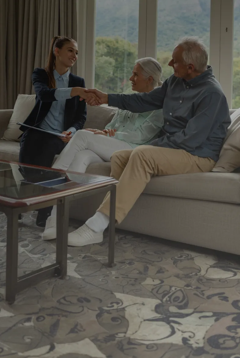 An adviser shaking hands with an older couple seated together on a sofa