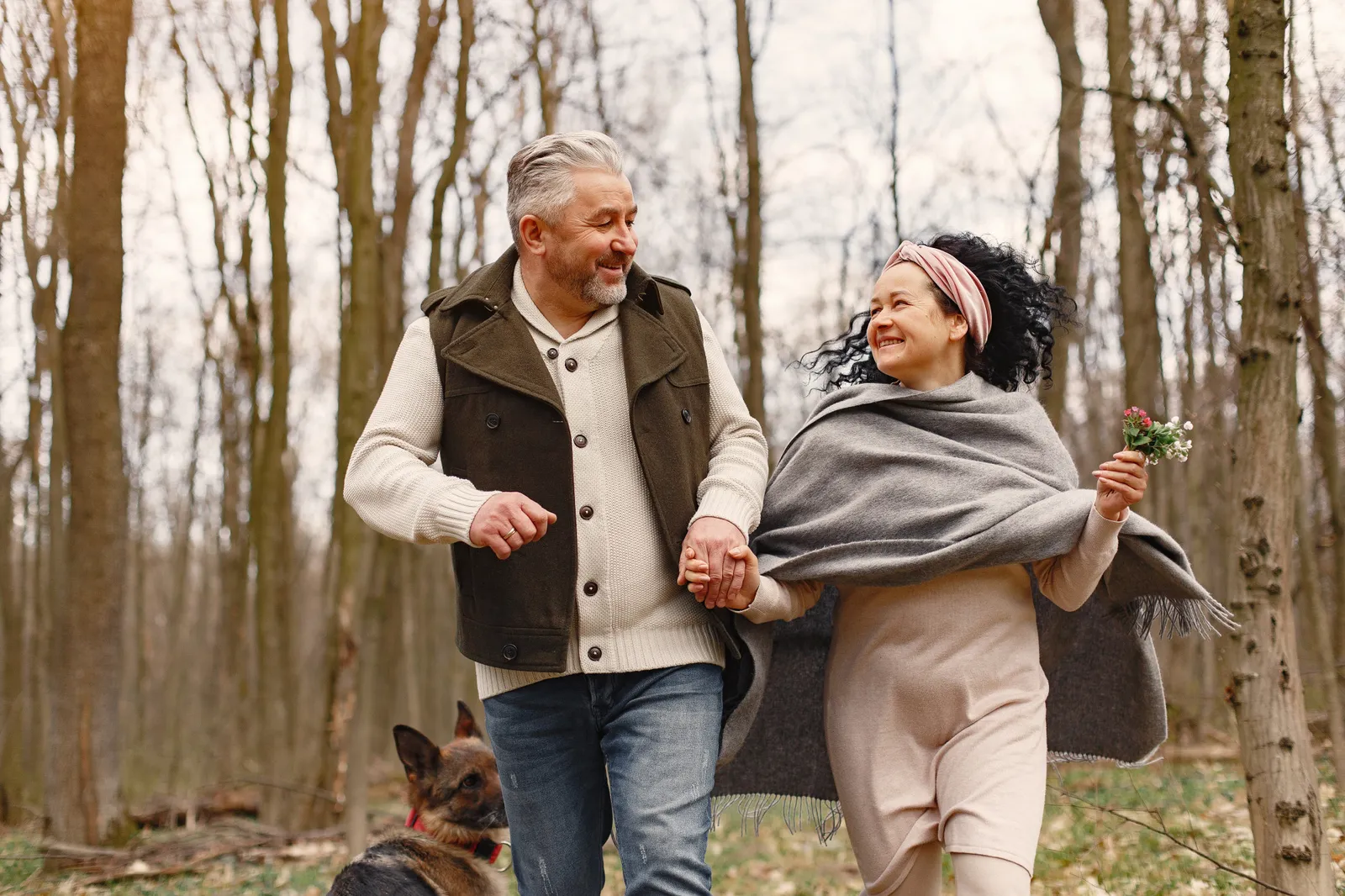 An older couple walking hand in hand through woodland