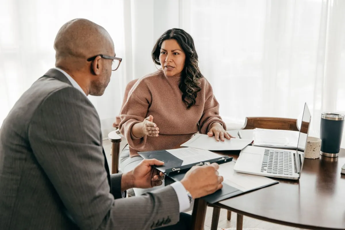 A woman talking with an advisor across a table spread with paperwork and a laptop
