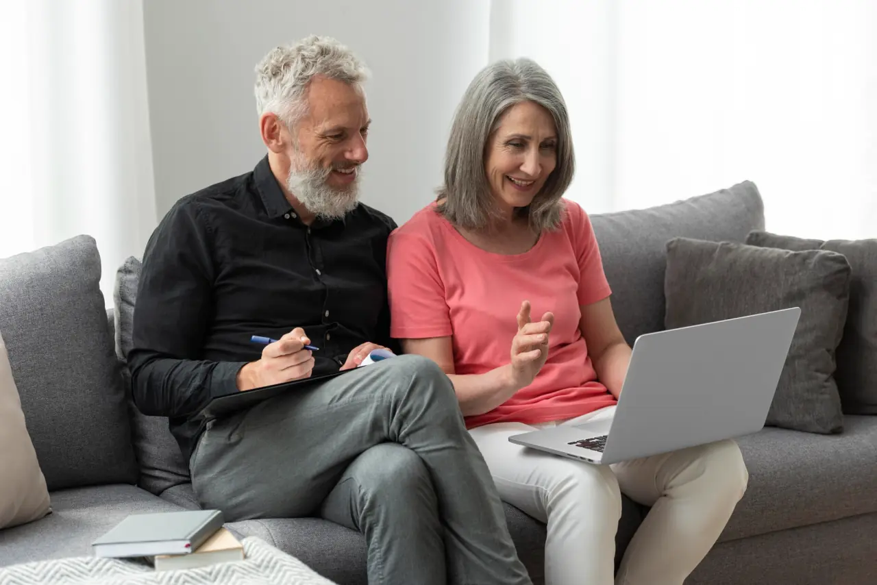 A couple in their sixties sitting on a sofa, going through retirement paperwork together on a laptop