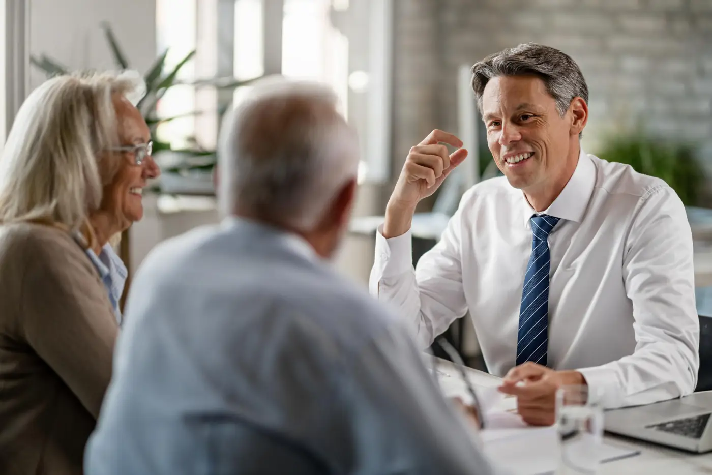 An adviser in a shirt and tie talking with an older couple across a desk