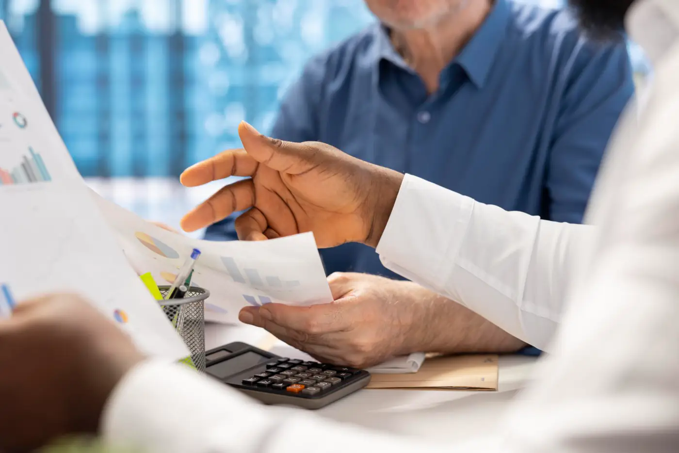 Hands holding a receipt over a calculator and printed charts on a desk