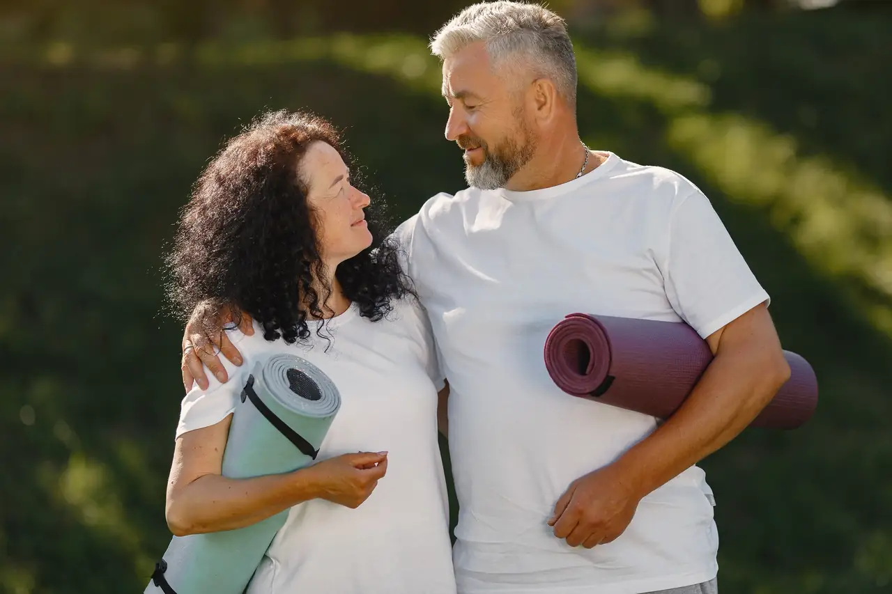 A couple in their sixties standing outdoors with their arms around each other, looking at one another