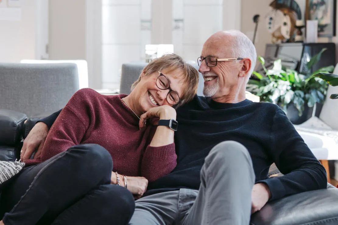 A smiling older couple sitting close together on a living-room sofa