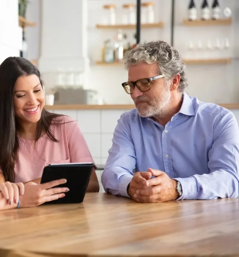 A woman showing a tablet to an older man across a kitchen counter