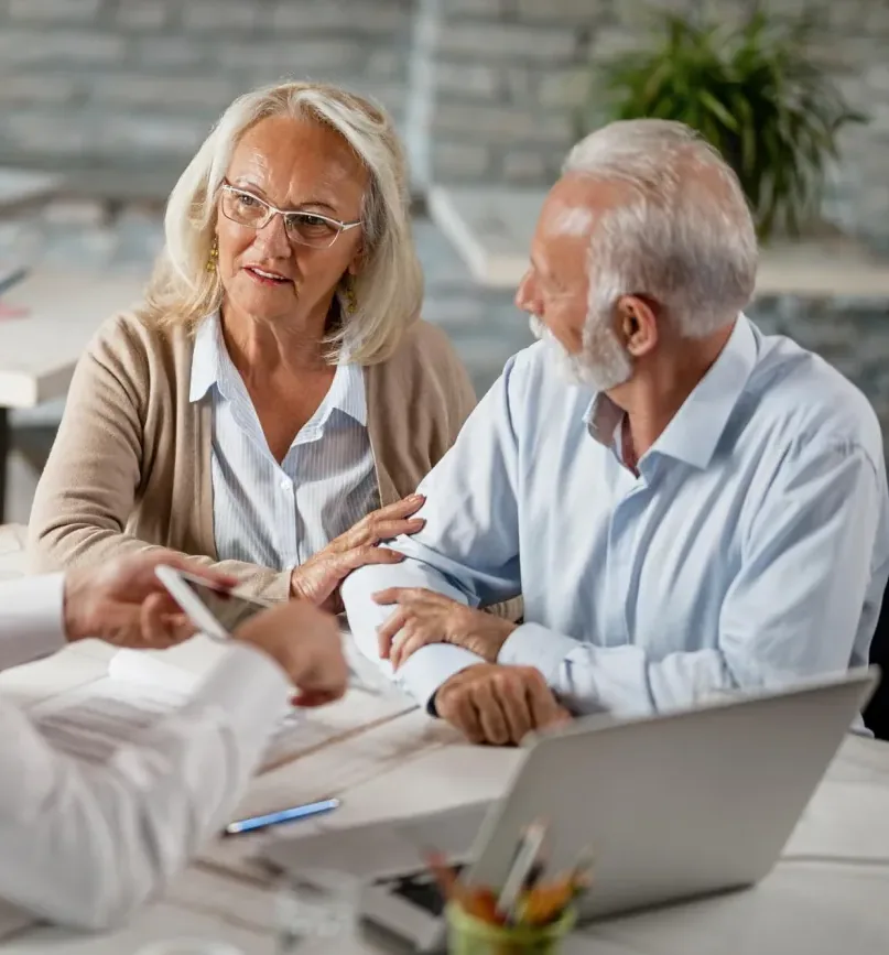 An advisor talking across a table with an older couple over printed paperwork