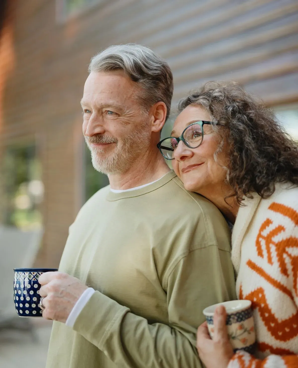 A retired couple standing close together outdoors, both looking into the distance